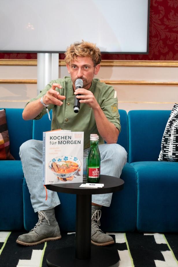 Ein Mann mit Mikrofon sitzt neben dem Buch „Kochen für Morgen“.