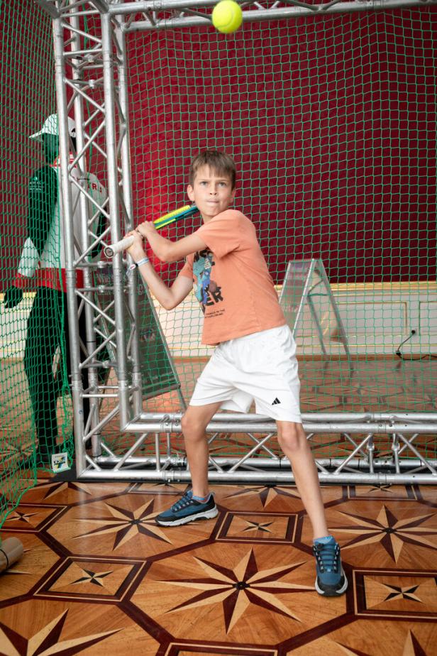 Ein Junge schlägt einen Tennisball mit einem Schläger in einer Halle.