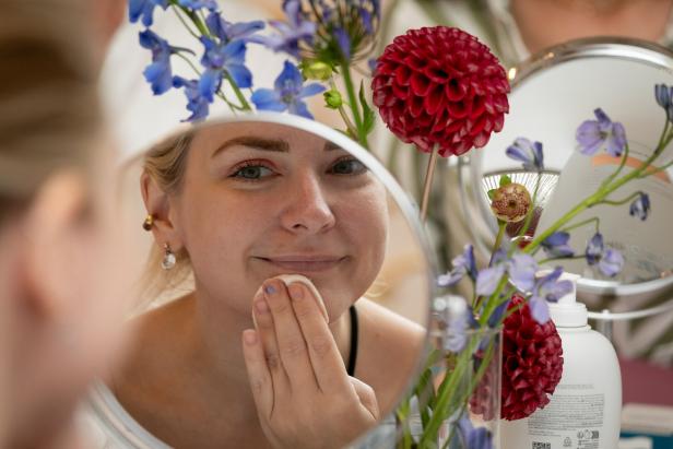 Eine Frau reinigt ihr Gesicht vor einem Spiegel, der mit Blumen geschmückt ist.
