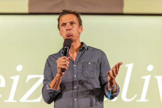 Ein Mann spricht mit einem Mikrofon in der Hand vor einem Publikum.