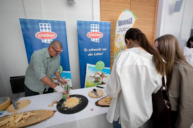 Ein Mann bereitet an einem Stand Käse der Marke Schärdinger für zwei Frauen zu.