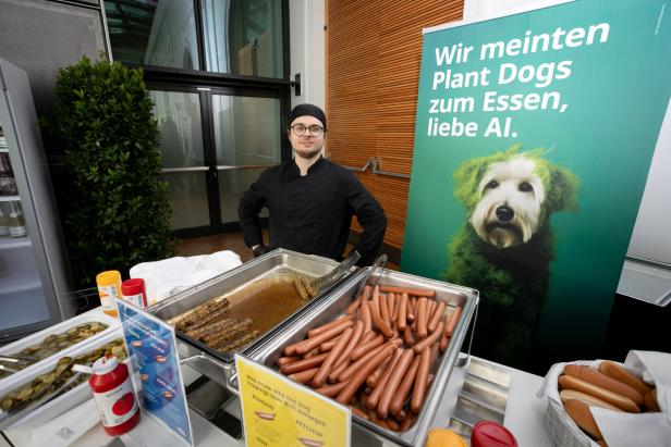 Ein Koch steht an einem Stand mit Hotdogs und einem Plakat mit der Aufschrift „Wir meinten Plant Dogs zum Essen, liebe AI.“.