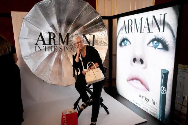 Eine ältere Frau posiert vor einem Armani-Werbeplakat und einem großen Reflektor.