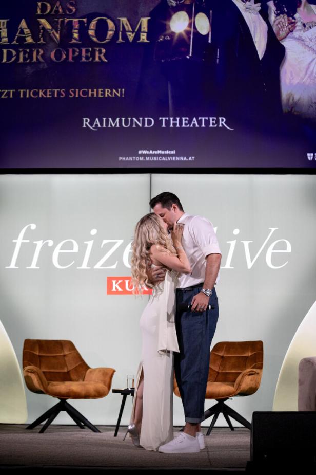 Ein Paar küsst sich vor einer Werbetafel für „Das Phantom der Oper“ im Raimund Theater.