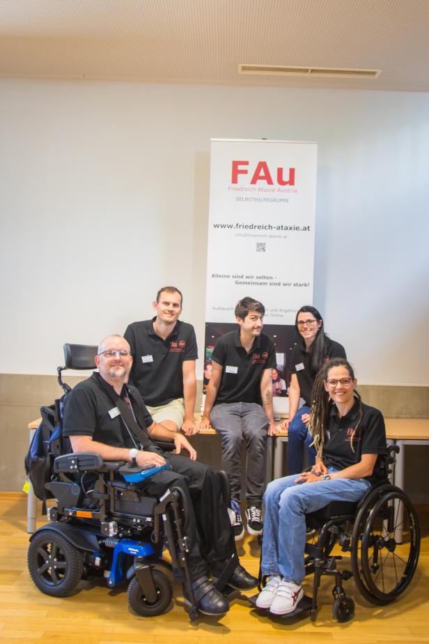 Mehrere Personen sitzen zum Teil im Rollstuhl zusammen und lächeln für ein Gruppenfoto.