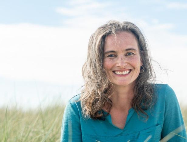 Eine lächelnde Frau mit langen, grauen Haaren steht im Gras.