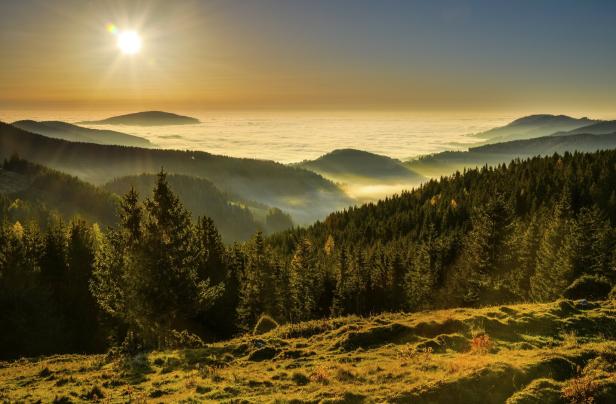 Die Sonne scheint über eine Hügellandschaft, die von Nebel bedeckt ist.