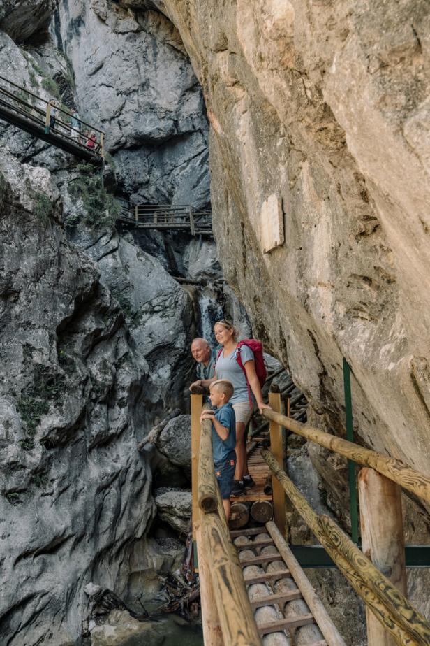Eine Familie wandert auf einem Holzsteg durch eine felsige Schlucht.