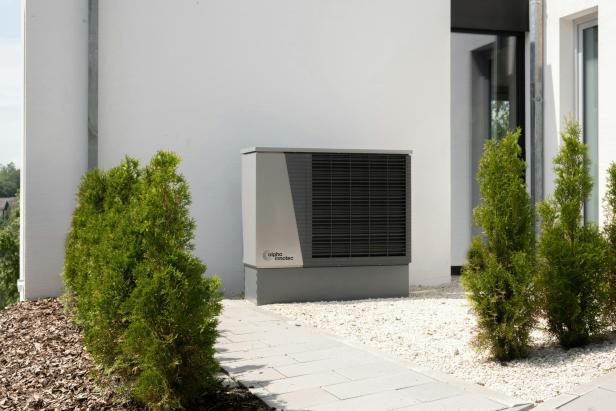 Eine Wärmepumpe von Alpha Innotec steht vor einer weißen Hauswand.