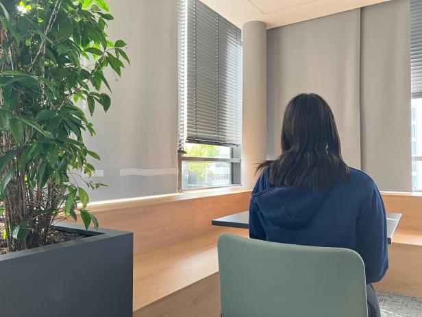 Eine Person sitzt in einem hellen Raum mit einem großen Fenster.