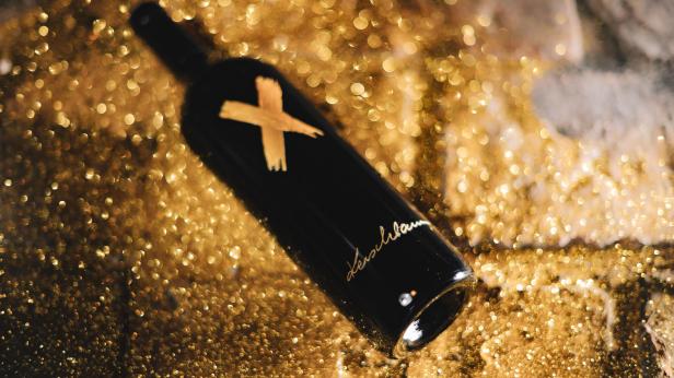 Eine schwarze Weinflasche von Weingut Kerschbaum liegt auf goldenem Glitter.