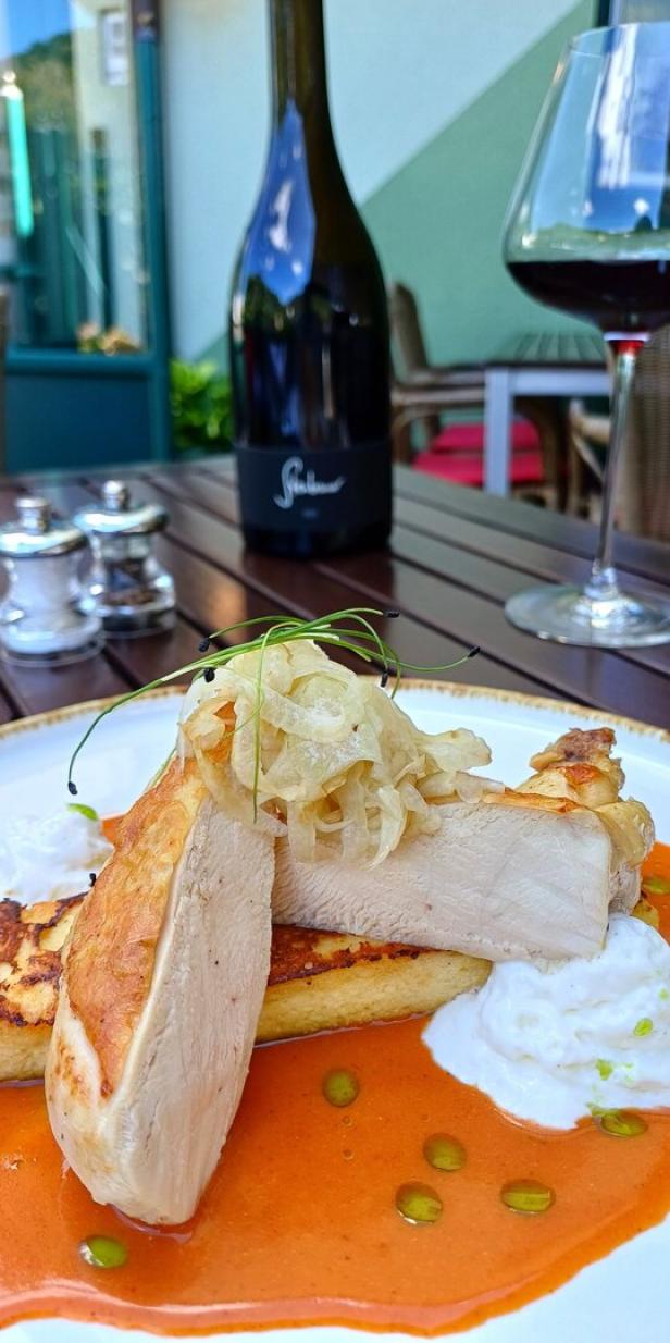 Hühnerfleisch angerichtet in einer Paprikasauce, im Hintergrund stehen ein Weinglas und eine Weinflasche. 