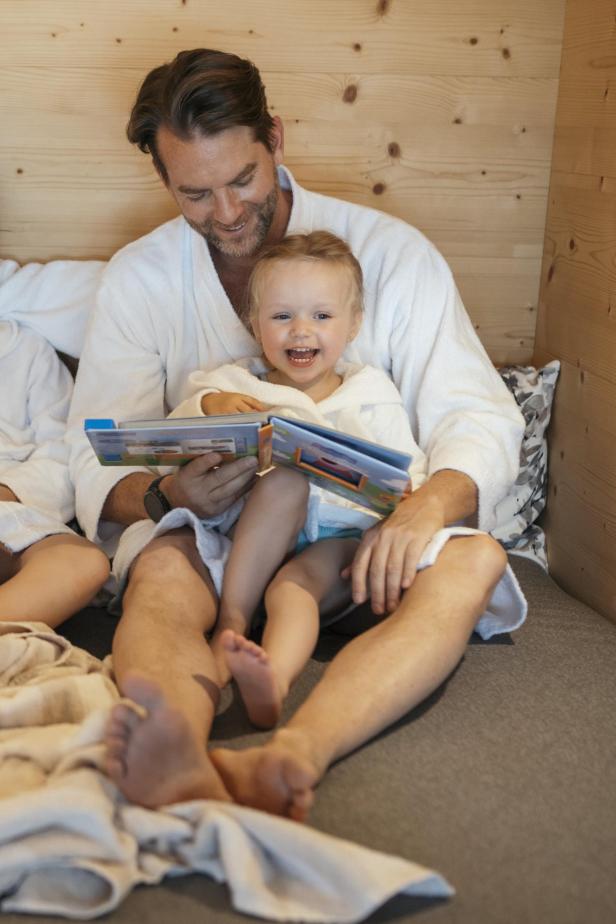 Ein Mann liest seinem Kleinkind im Bademantel vor. 