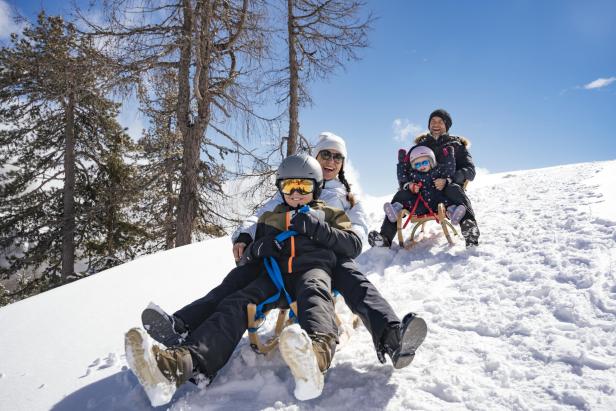 Eine Familie fährt einen schneebedeckten Berg mit Schlitten runter. 
