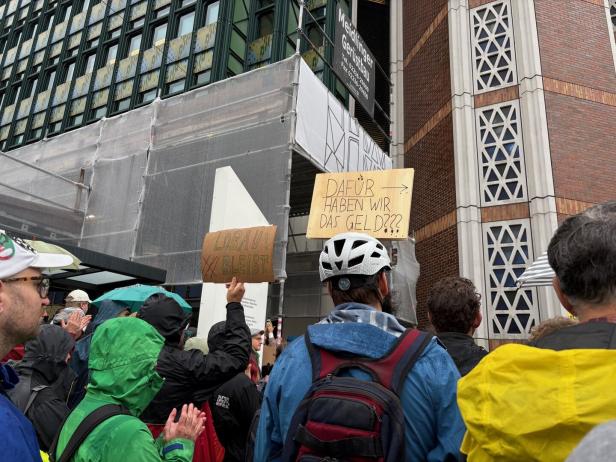 Demonstranten halten Schilder mit Aufschriften wie "Lobau bleibt" und "Dafür haben wir das Geld???" vor einem Gebäude hoch.