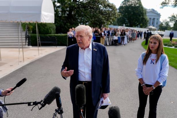 Donald Trump spricht vor Mikrofonen, während Kai Trump daneben steht und im Hintergrund eine Menschenmenge zu sehen ist.