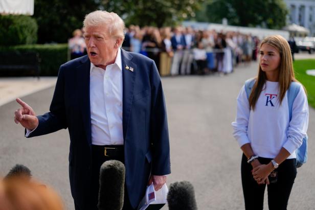 Donald Trump spricht vor Mikrofonen, während Kai Trump daneben steht und im Hintergrund eine Menschenmenge zu sehen ist.