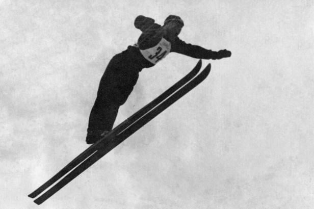 Skispringer Bubi Bradl springend auf dem Holmenkollen mit Mütze. 