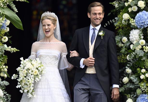 Ein lachendes Brautpaar - es sind Prinzessin Marie Caroline von und zu Liechtenstein und Leopoldo Maduro Vollmer - verlässt Arm in Arm eine festlich mit weißen und blauen Blumen geschmückte Location.