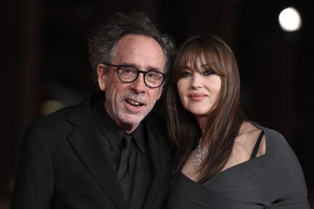 Tim Burton und Monica Bellucci posieren nebeneinander vor einem dunklen Hintergrund.