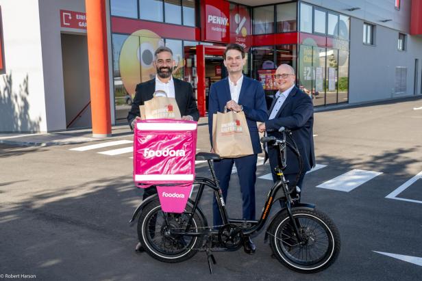 Foodora-Chef Gaied und die Penny-Geschäftsführer Karras und Greller mit Foodora-Fahrrad vor Penny-Filiale