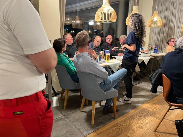 Eine Gruppe Menschen sitzen um einen Tisch in der Donaulodge. Ein Mann im grauen Hemd spricht in das ORF-Mikrofon.