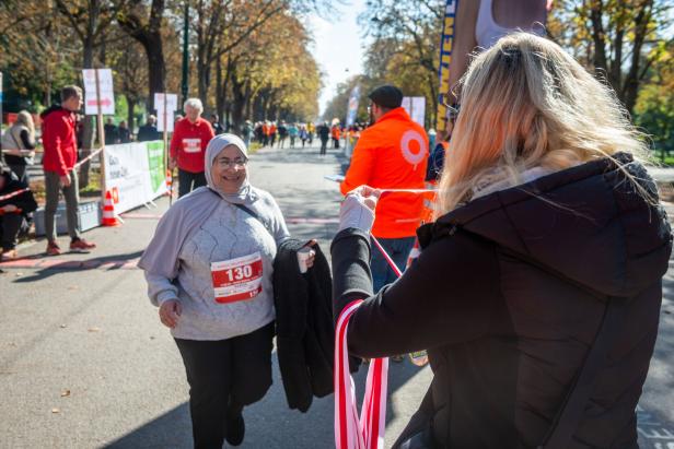 Eine Frau mit Startnummer läuft lächelnd auf eine Helferin zu, die Medaillen bei einer Laufveranstaltung verteilt.
