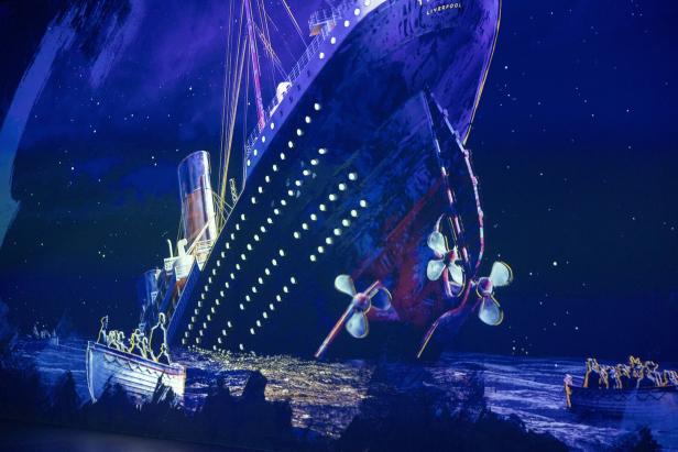 Die Titanic sinkt nachts im Meer, während Menschen in Rettungsbooten auf dem Wasser treiben.