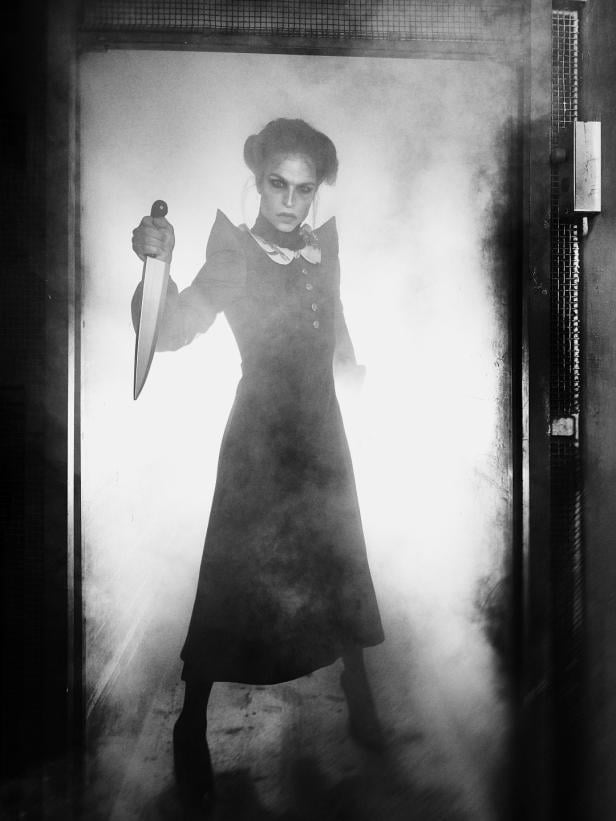 Tamara Mascara steht in dunkler Verkleidung mit erhobenem Messer in nebliger Kulisse und inszeniert eine Szene inspiriert von Hitchcocks „Psycho“.