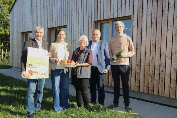 Eine Gruppe von fünf Personen posiert mit Äpfeln und einer Flasche vor einem Holzgebäude.