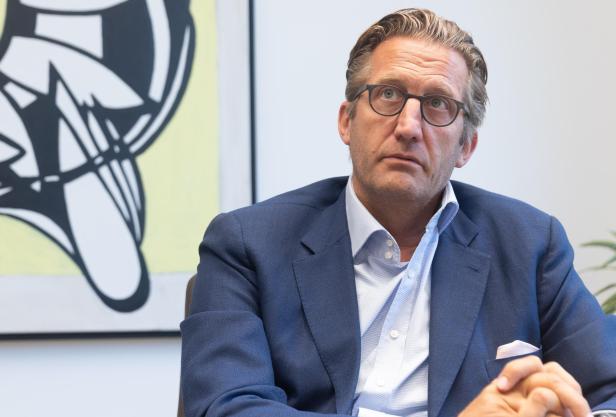 Ein Mann mit Brille, hellblauem Hemd und dunkelblauem Sakko blickt nachdenklich nach oben.