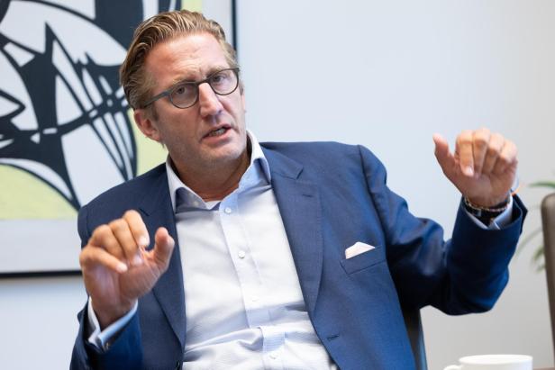 Zöchling im blauen Anzug und mit Brille gestikuliert bei einem Gespräch.