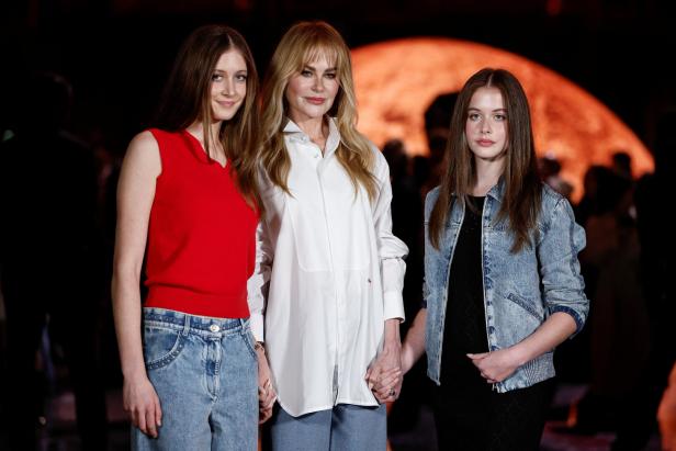 Nicole Kidman steht mit ihren Töchter Sunday und Faith Händchen haltend vor einem dunklen Hintergrund.