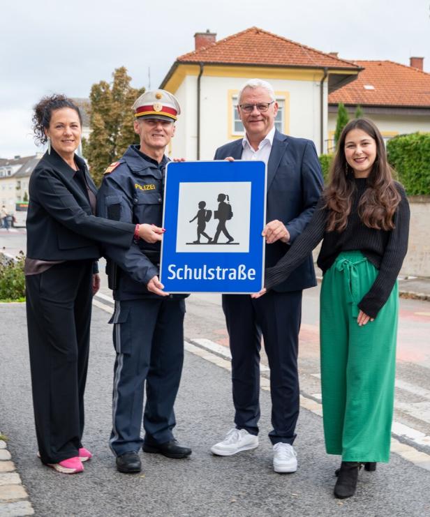 Vier Personen, darunter ein Polizist, halten ein blaues Schild mit der Aufschrift "Schulstraße".