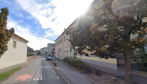 Die Bahnstraße mit bunten Blumen führt an einem gelben Gebäude vorbei.