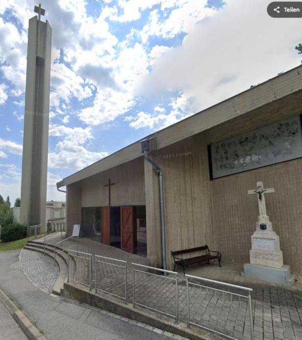 Eine Kirche mit einem hohen Turm und einem Kreuz vor dem Eingang ist zu sehen.