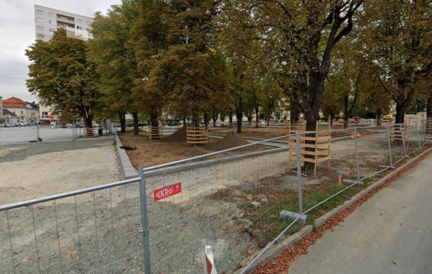 Ein Platz mit Bäumen wird durch einen Bauzaun und Holzkonstruktionen geschützt.