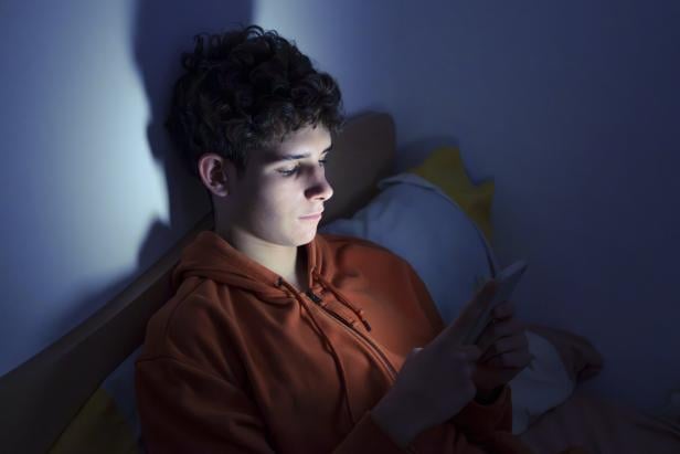 Teenager using a smartphone lying in bed late at night Teenager using a smartphone lying in bed late at night