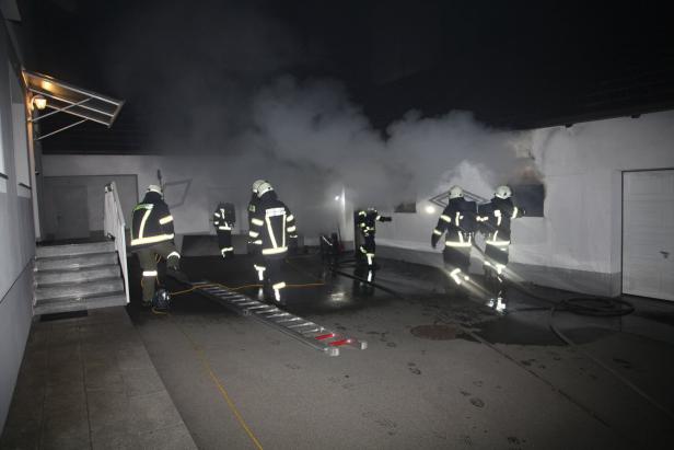 Mehrere Feuerwehrleute in Schutzkleidung sind nachts im Einsatz vor einem verrauchten Gebäude.
