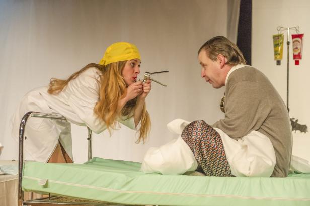 Eine Frau in Arztkleidung untersucht einen Mann mit einem Spekulum auf einer Krankenhausliege.