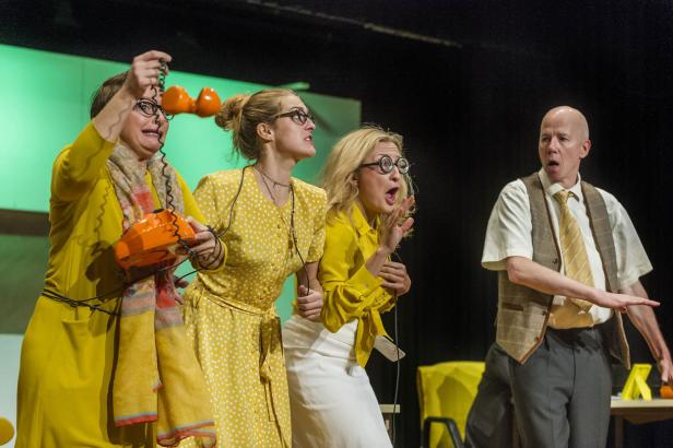 Vier Schauspieler auf einer Bühne mit überraschten Gesichtsausdrücken und einem orangefarbenen Telefon.