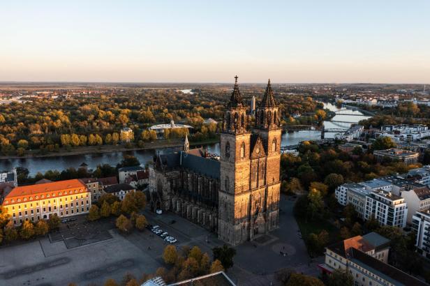 Luftaufnahme des Magdeburger Doms mit der Elbe im Hintergrund, umgeben von städtischer Architektur.
