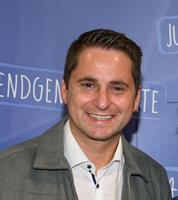 Mann mit weißem Hemd und grauer Jacke vor lila HIntergrund