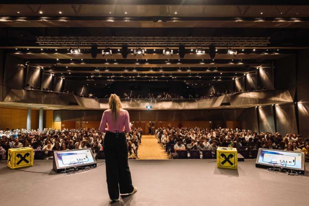 Raiffeisenlandesbank Burgenland. Eine Frau steht auf einer Bühne und spricht vor einem großen, voll besetzten Auditorium.