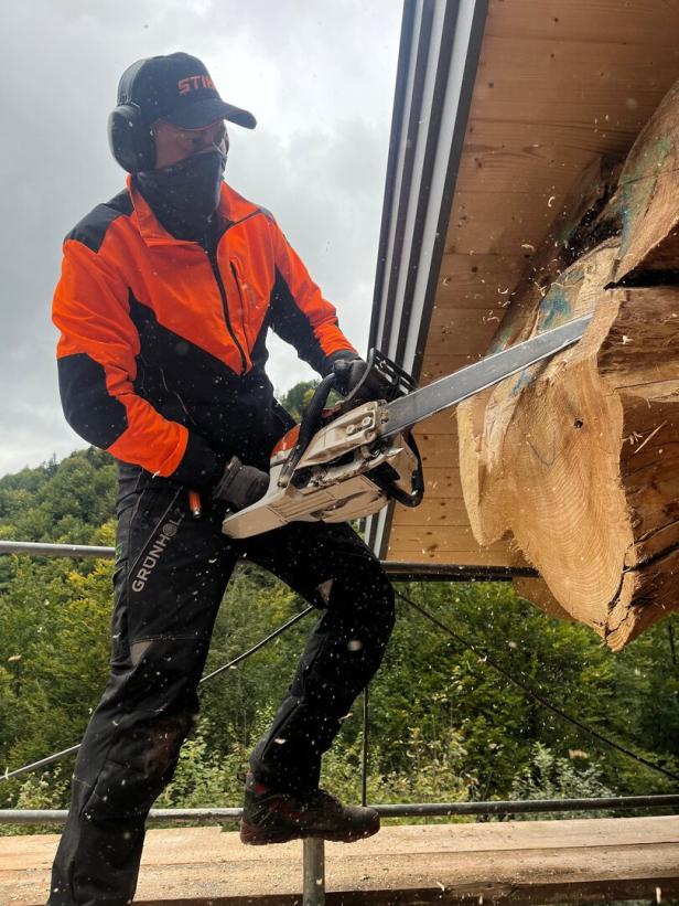 Ein Mann in Schutzkleidung bearbeitet einen großen Holzstamm mit der Motorsäge.