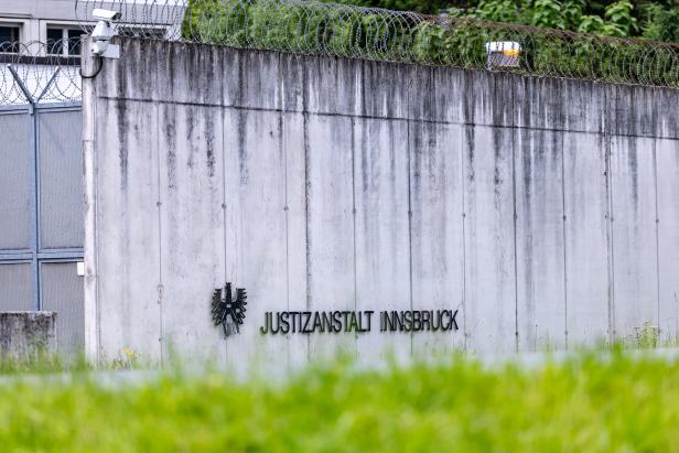 Eine graue Betonmauer mit Stacheldraht und der Aufschrift "Justizanstalt Innsbruck" ist zu sehen.