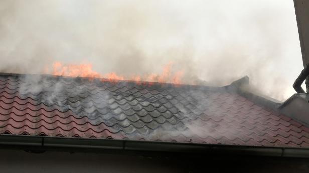 Eine Nahaufnahme von dem Dach, ein teil der Ziegel ist schwarz, Flammen züngeln am First.
