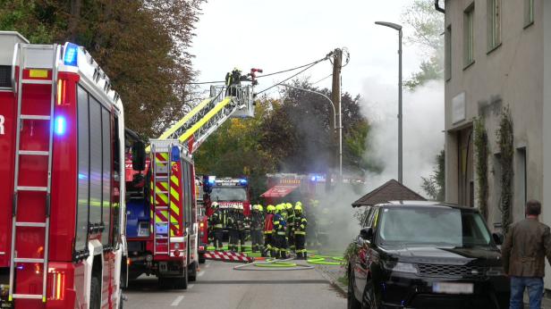 Eine Aufnahme von mehreren Feuerwehrautos, die hintereinander entlang der Straße geparkt sind, mittig sind eine Gruppe Feuerwehrmenschen in Uniform zu sehen.