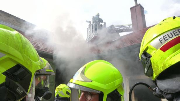 Eine Aufnahme von dem in Rauch gehüllten Wohngebäude, im Fokus stehen mehrere neongelbe Feuerwehrhelme.