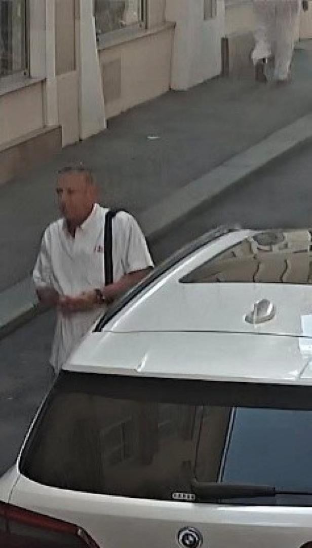 Ein Mann mittleren Alters in einem weißen Hemd steht neben einem weißen Auto.